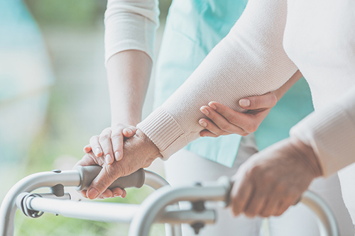 Close up of an elderly woman's hands on top of her walker with a younger woman's hands assisting her